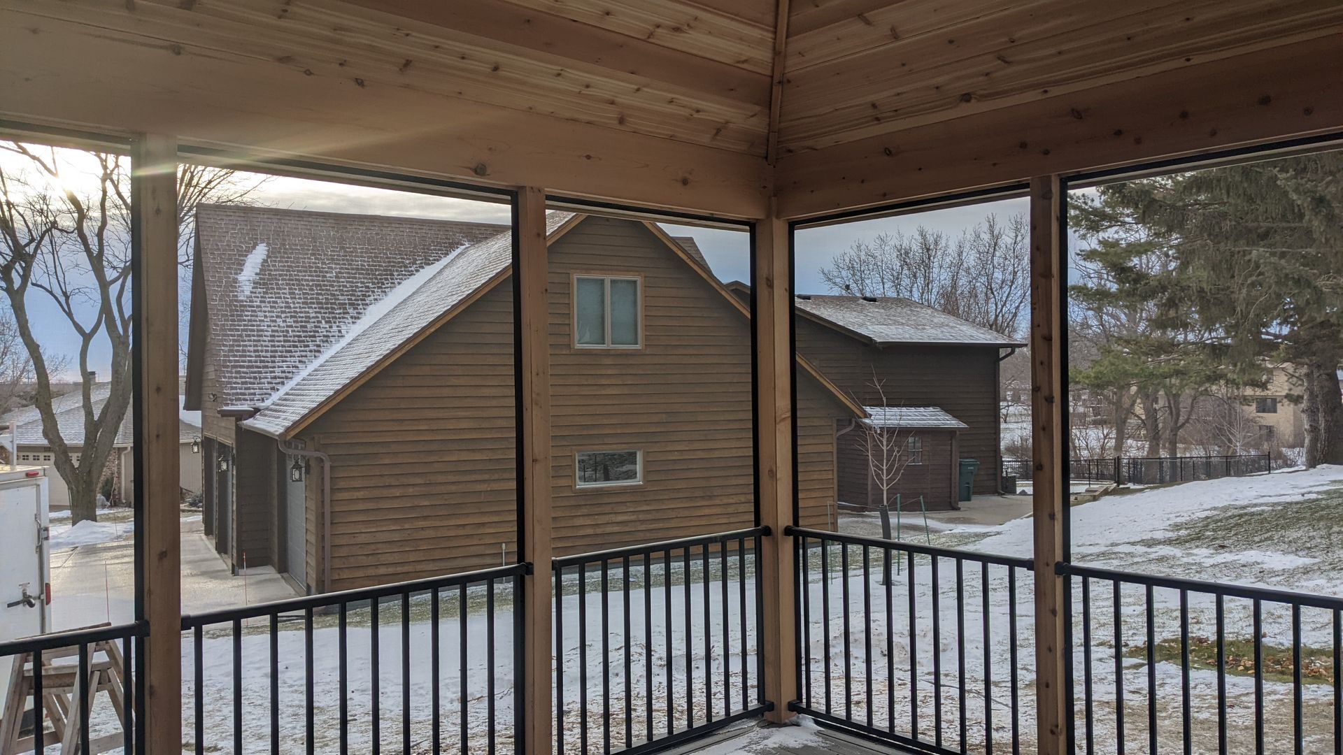 A screened in porch with a view of a snowy yard and a house.