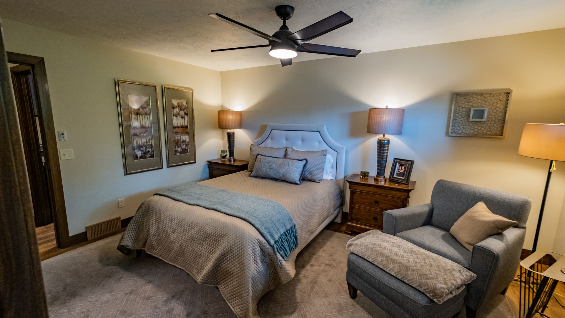 A bedroom with a bed, chair, nightstand, lamp and ceiling fan.
