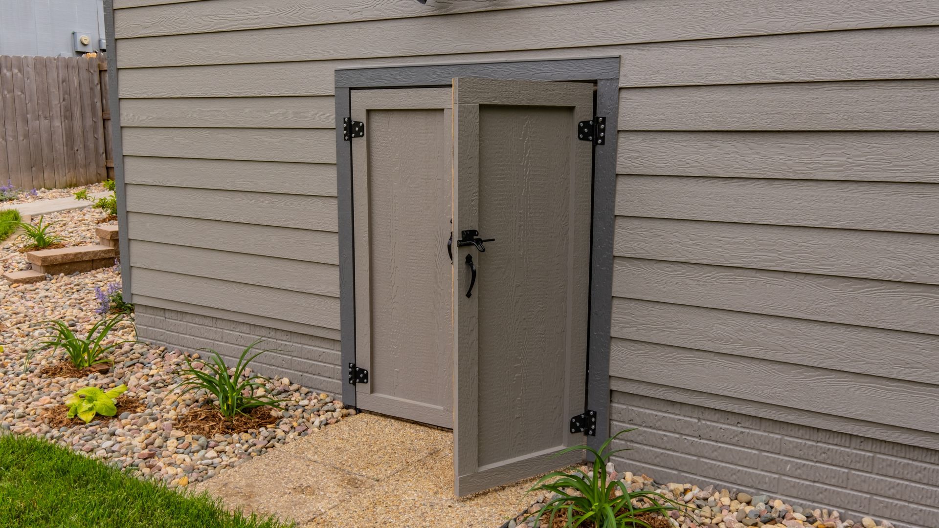 A gray door is open on the side of a house.