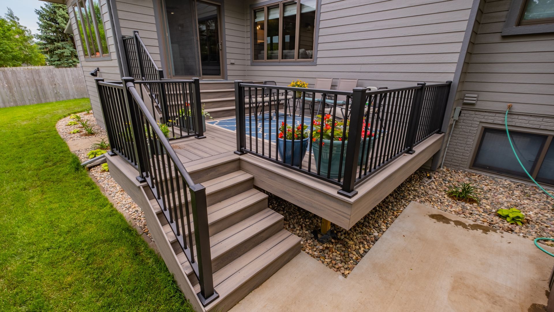 There is a deck with stairs leading up to it and a pool in the background.
