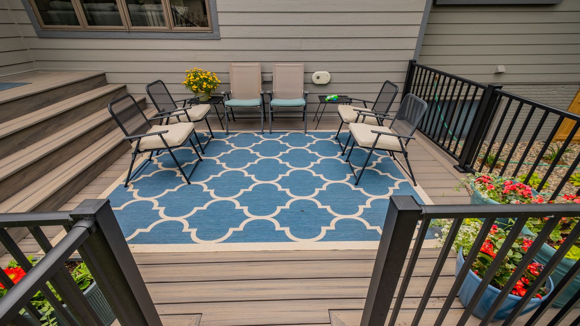 A deck with a blue rug and chairs on it.