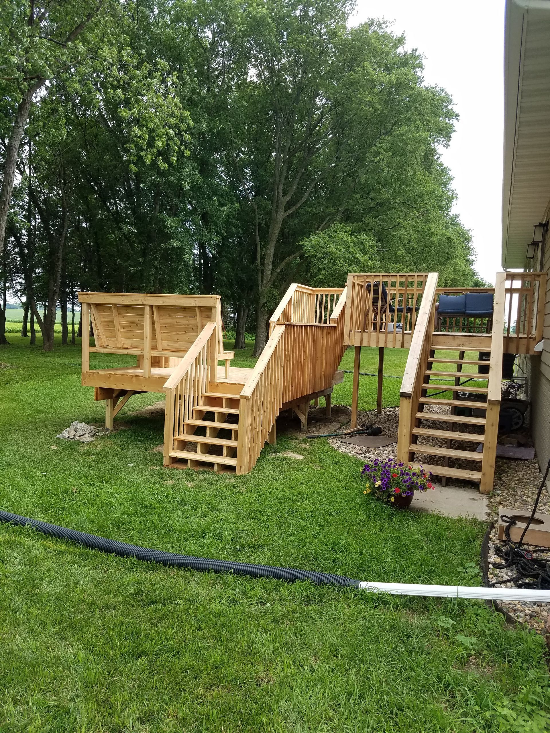 A wooden deck with stairs and a bench in the backyard of a house.