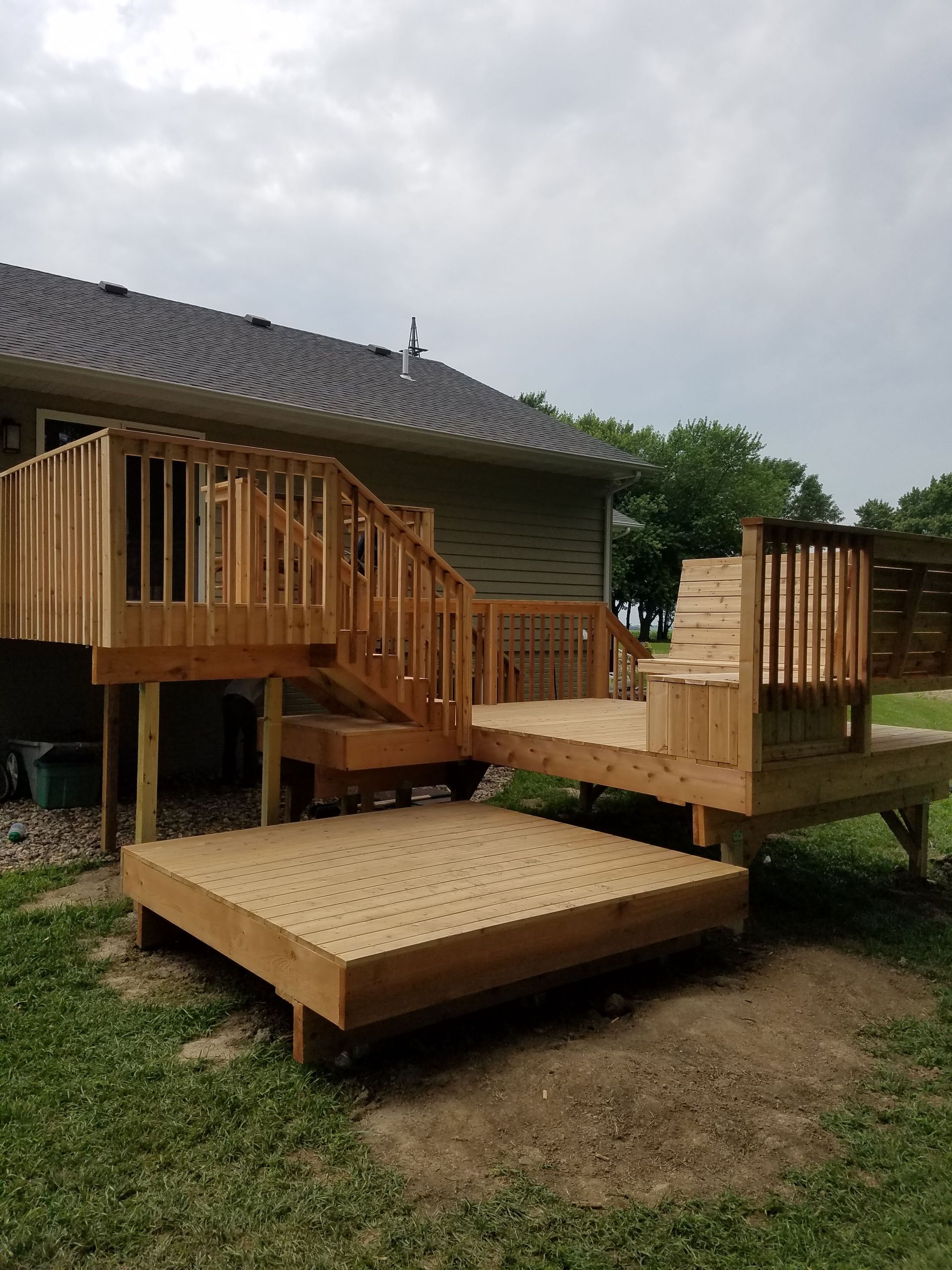 A wooden deck with stairs is sitting in the grass in front of a house.