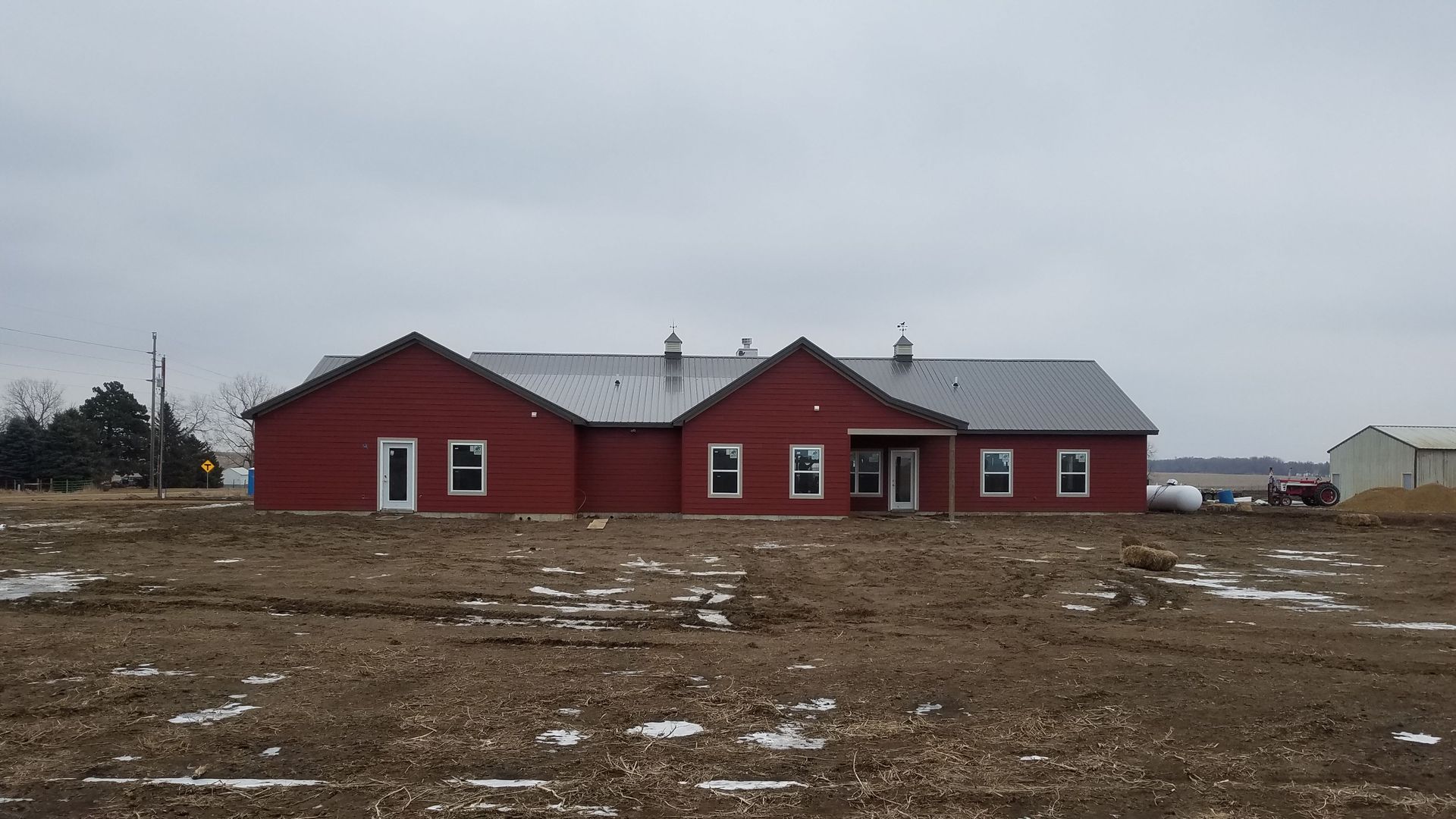 A large red barn is sitting in the middle of a dirt field.