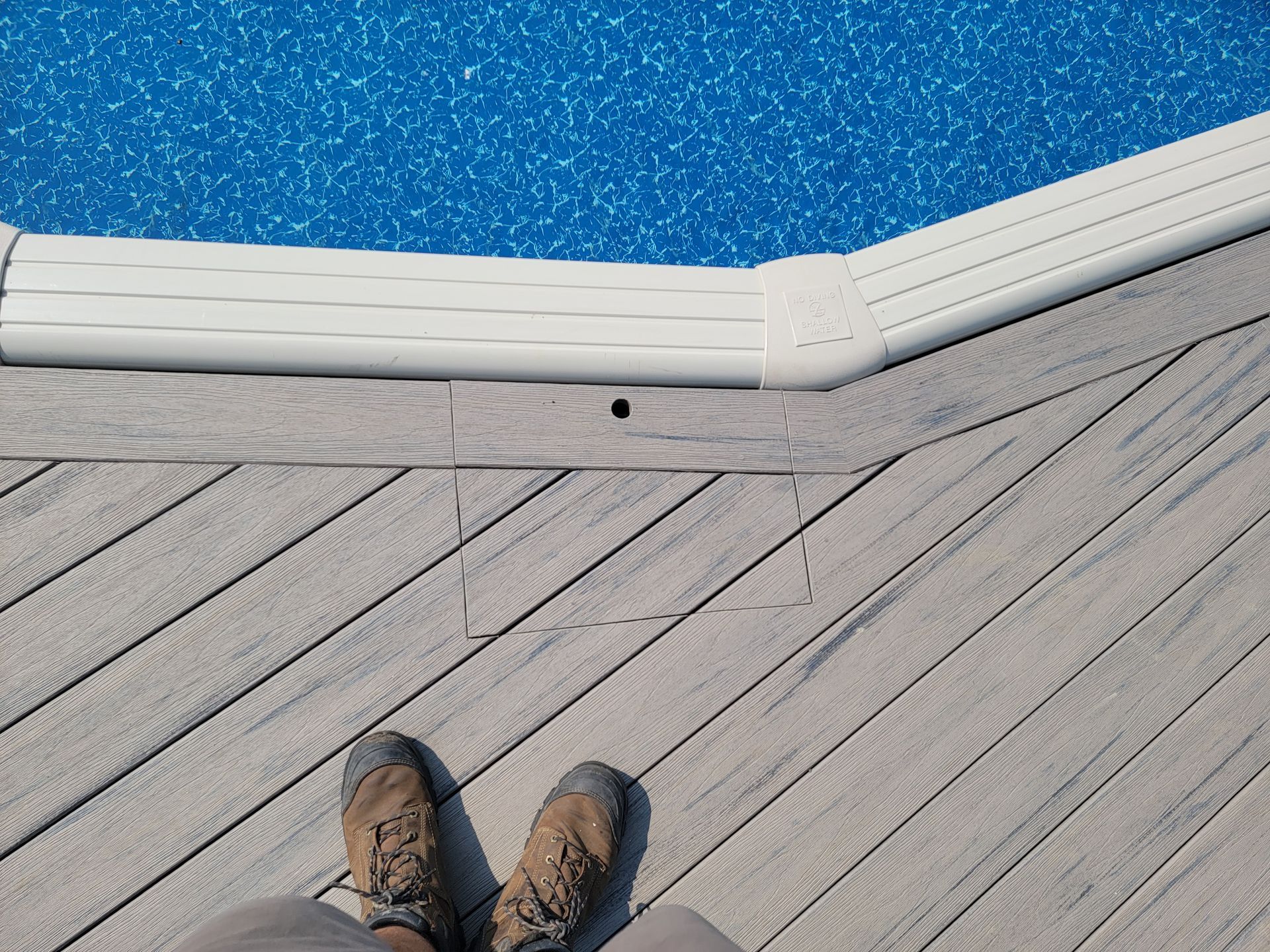 A person is standing on a wooden deck next to a pool.