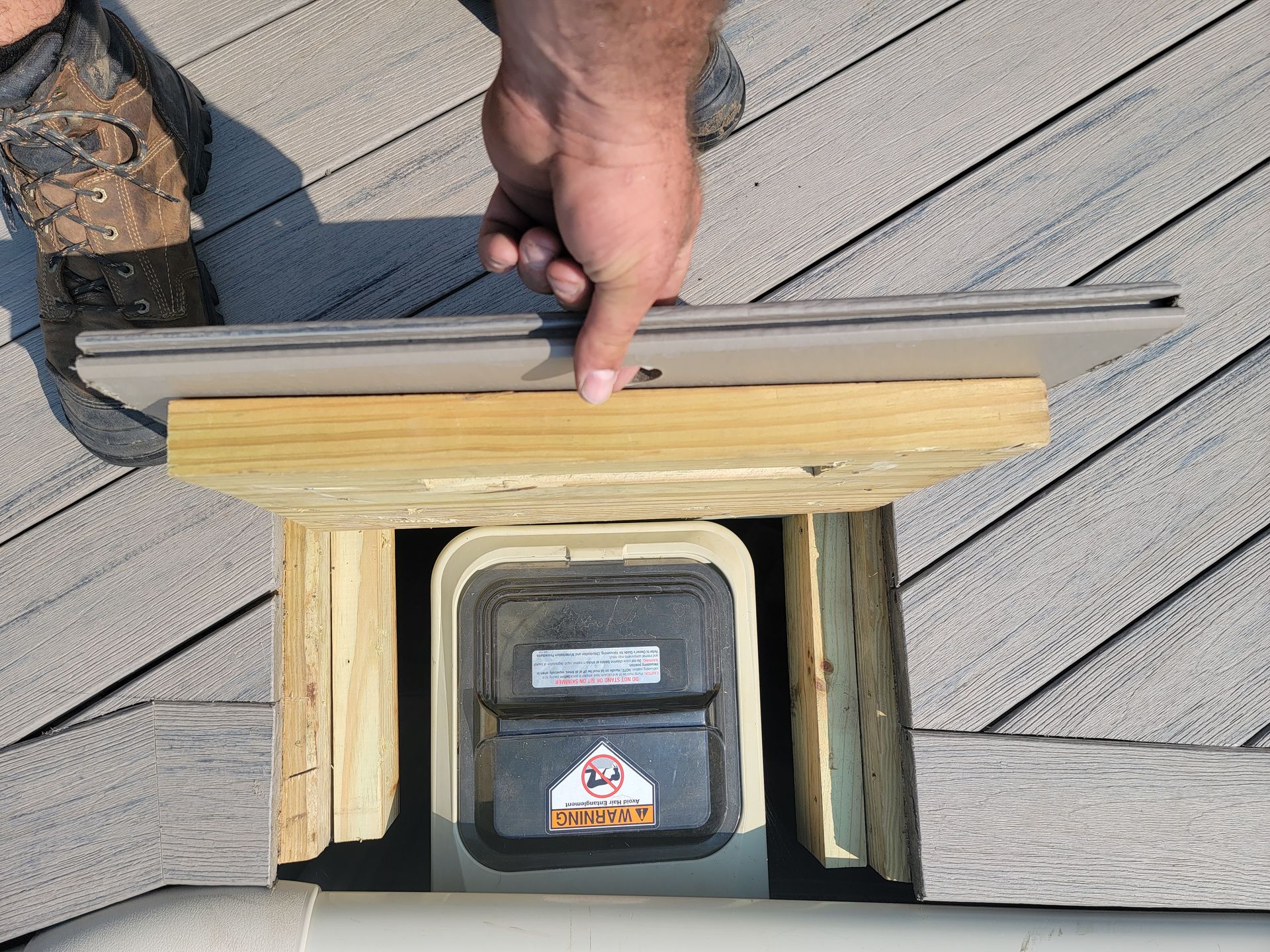 A person is holding a piece of wood over a trash can on a deck.