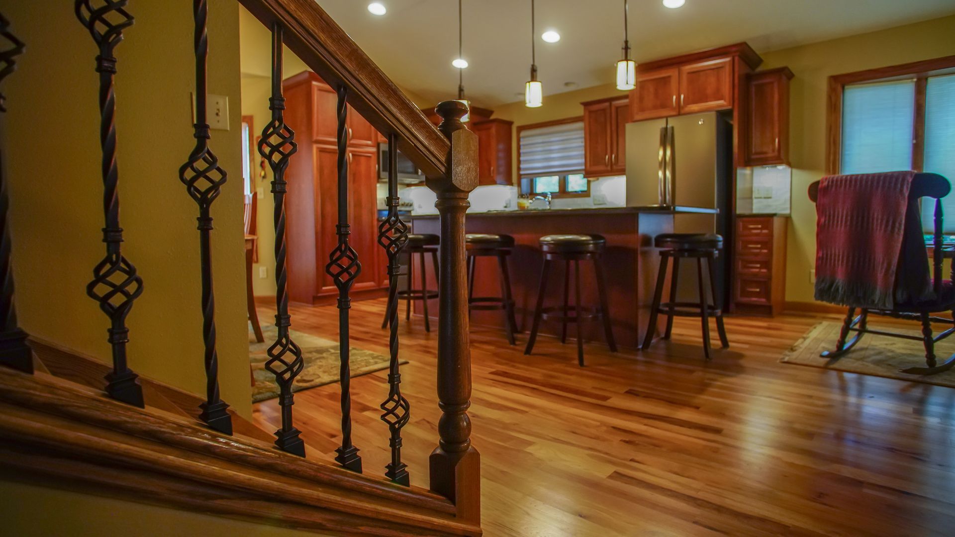 A wooden staircase leading up to a kitchen with a wrought iron railing.