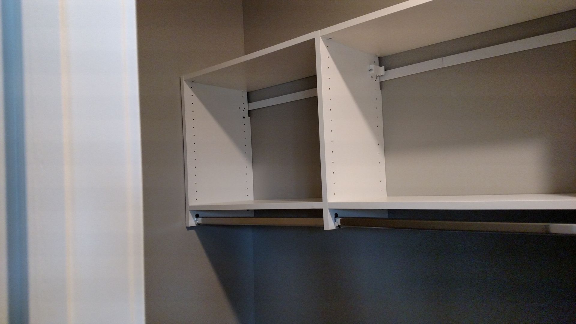 A walk in closet with white shelves and a hanging rail.
