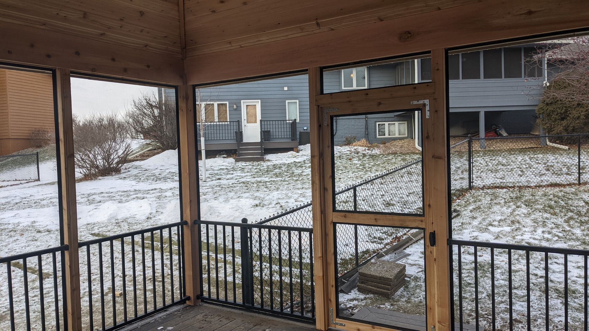 A screened in porch with snow on the ground and a house in the background.