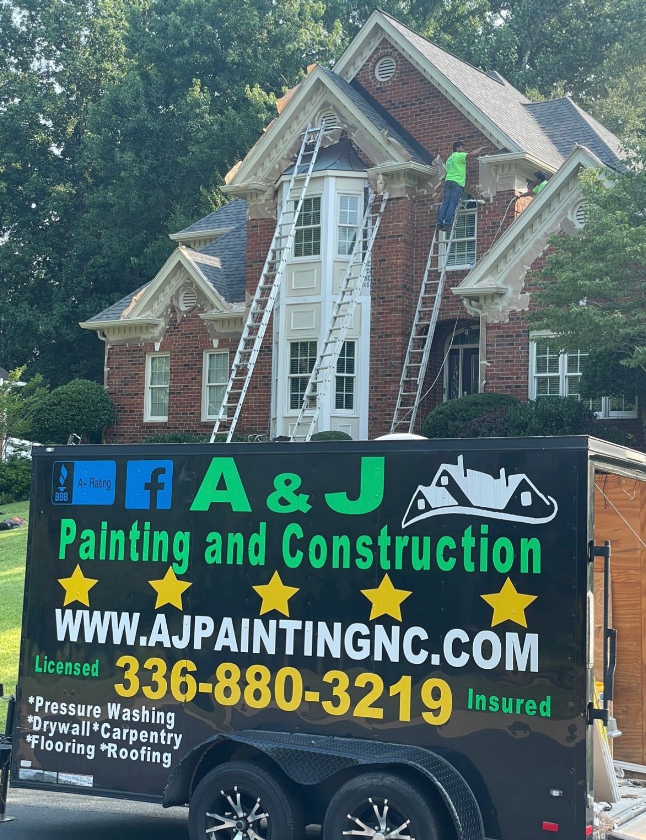 A trailer for A & J Painting and Construction is parked in front of a brick house