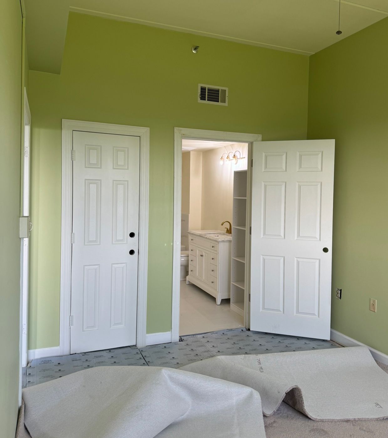 A room with green walls and white doors leading to a bathroom