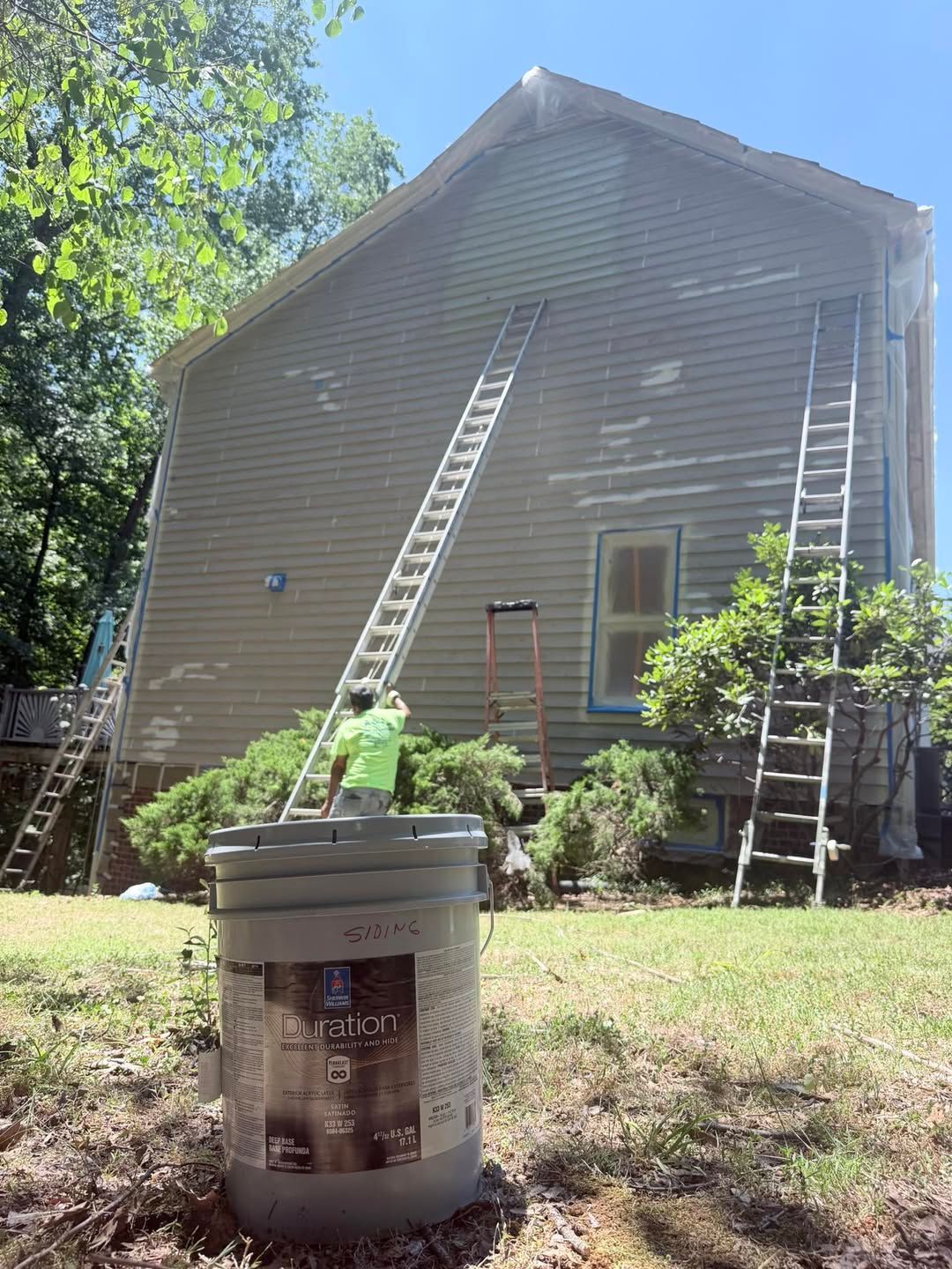 Workers on ladders painting the exterior of a tan house on a sunny day.