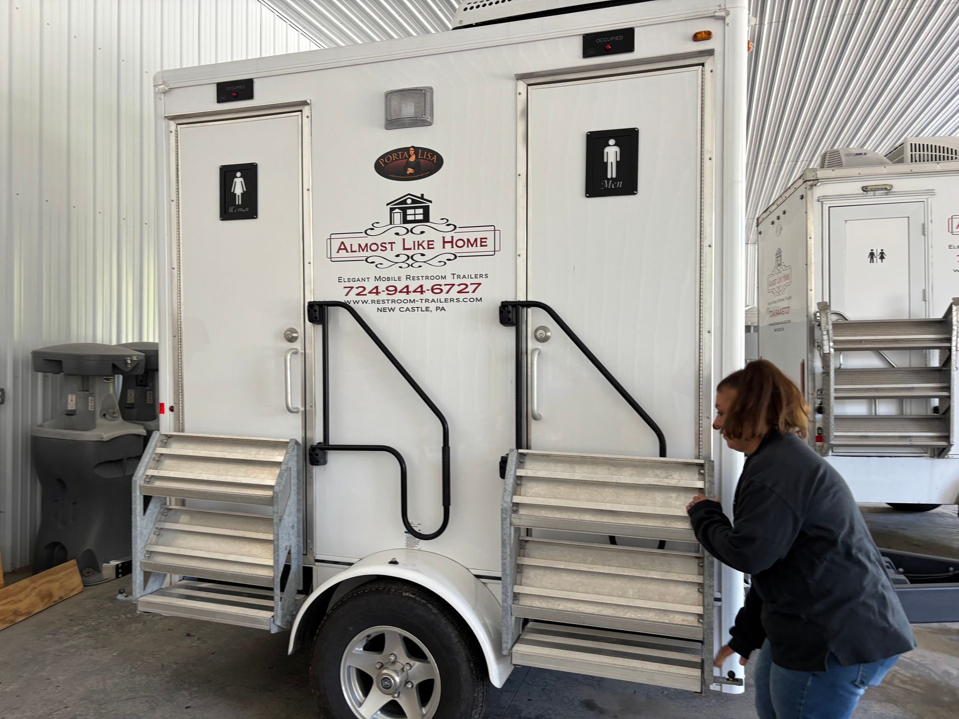 Portable restroom trailer in a warehouse, with a person opening the side door.