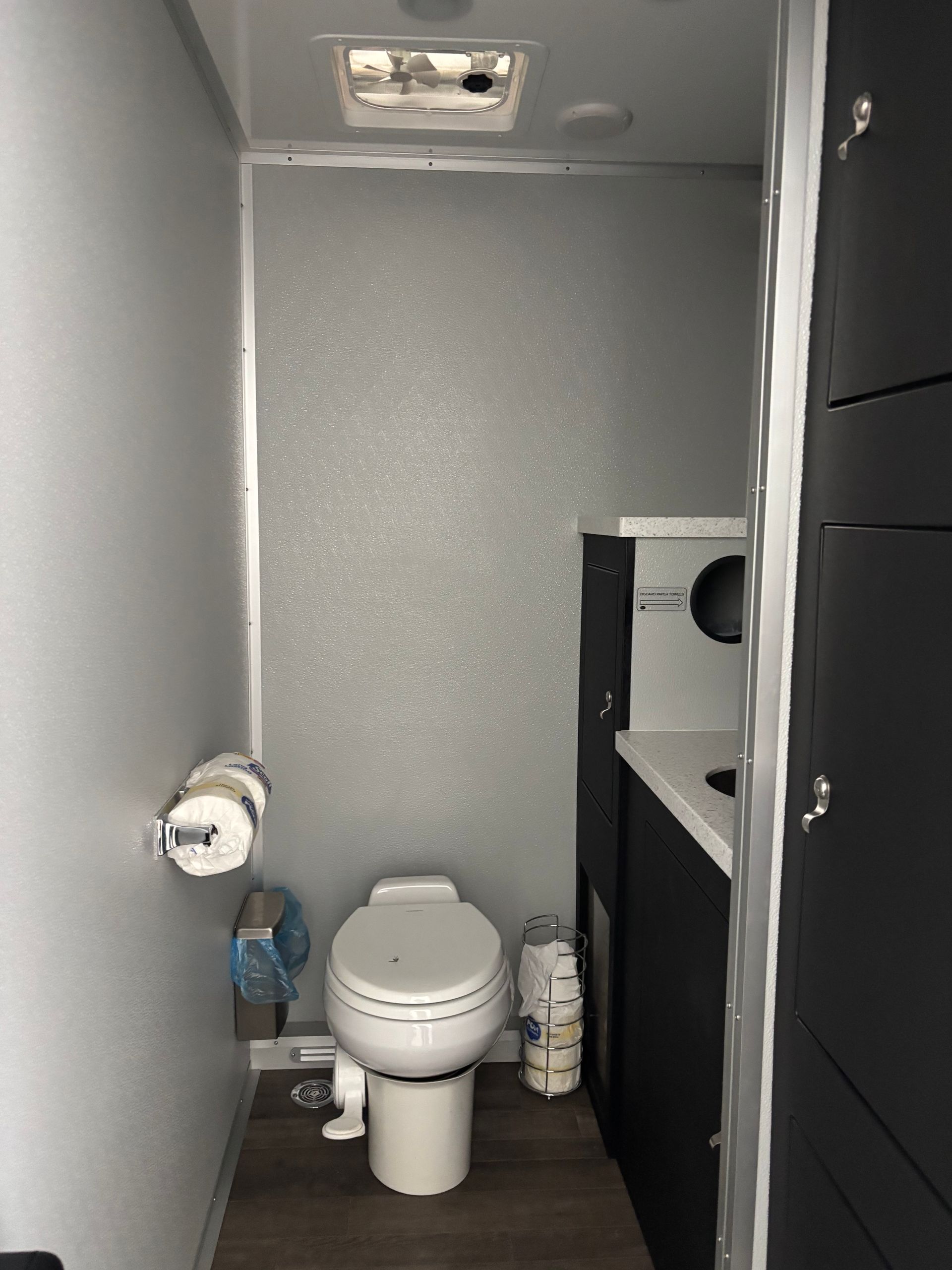 Small gray restroom with a toilet, sink, toilet paper holder, and ceiling vent.