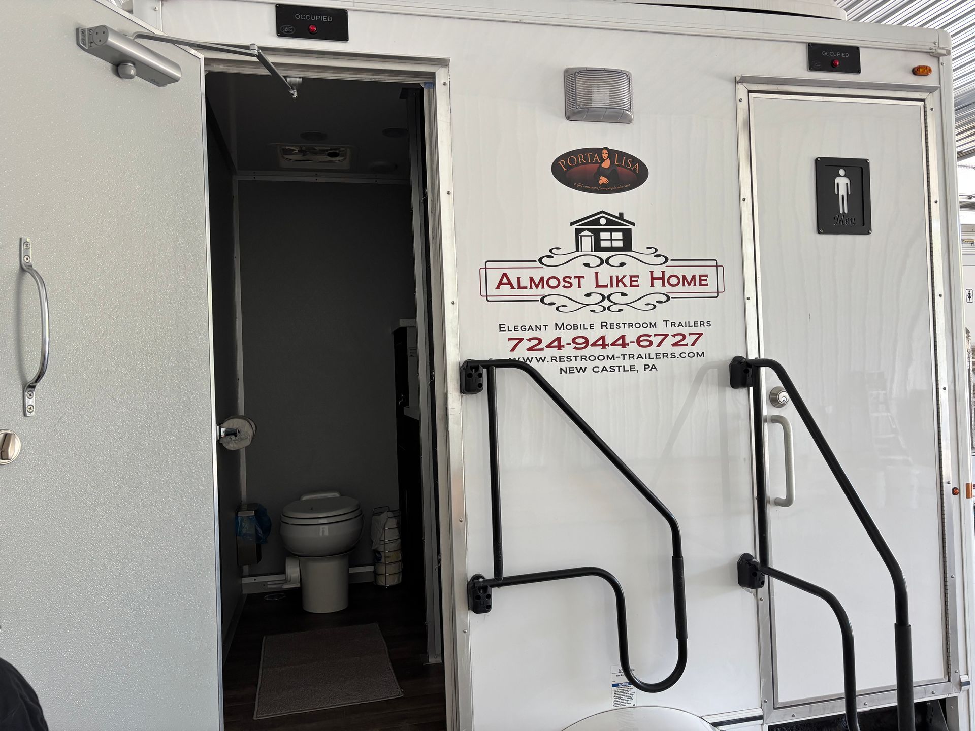 White trailer restroom entrance with handicap rails and an 