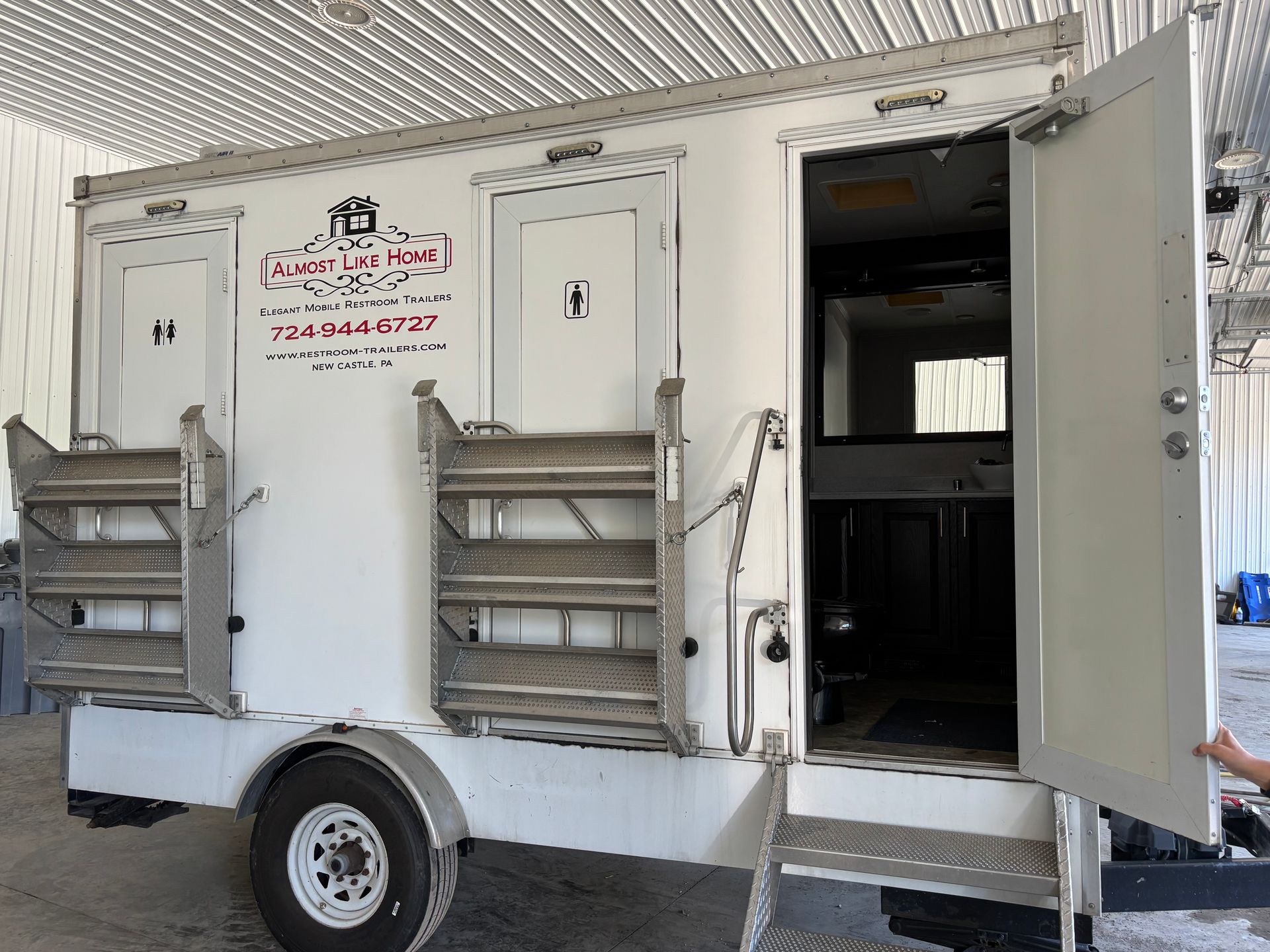 White utility trailer with side compartments and an open side door inside a garage-like space