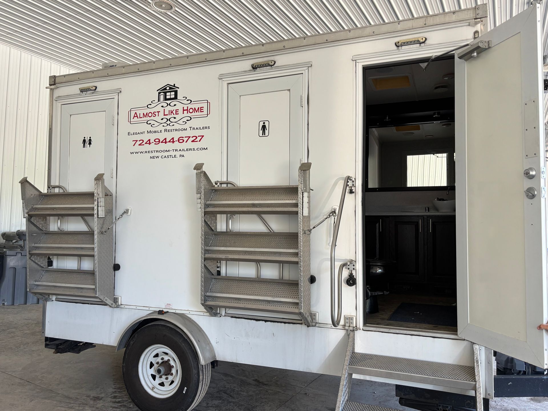 Small white food trailer with serving windows and an open side door, parked under a covered area