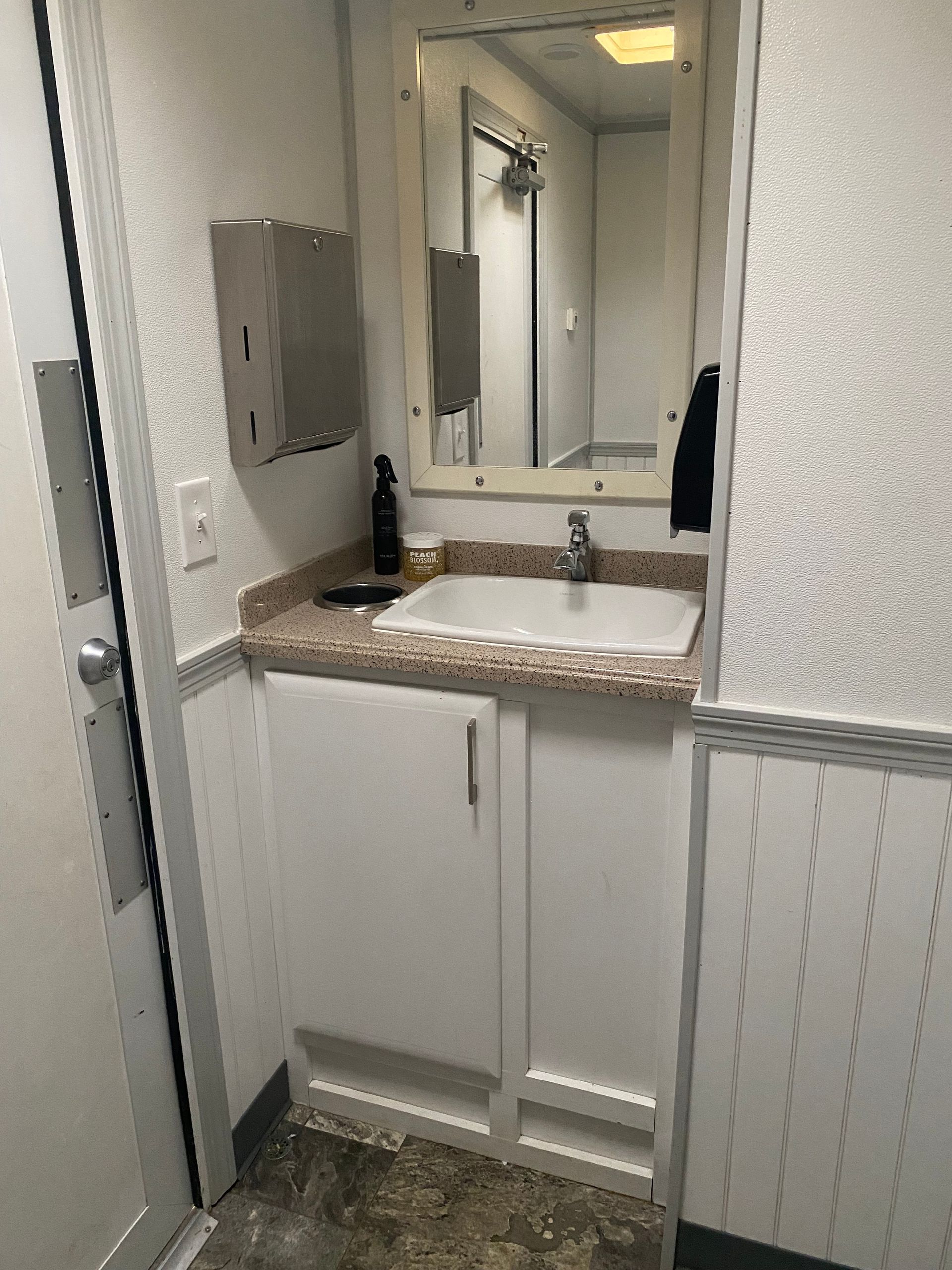 Small bathroom vanity with sink, mirror, and countertop in a narrow white-tiled room.