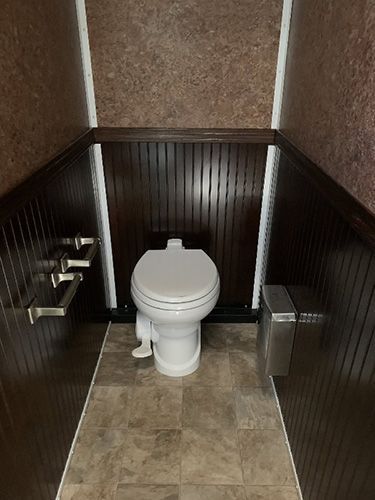 Small restroom stall with a toilet, dark wainscoting, and tiled floor.