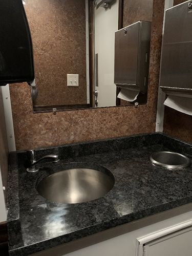 Public restroom sink with black countertop, round stainless basin, mirror, and soap dispenser