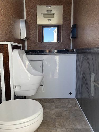 Small restroom with a white toilet, tiled walls, sink, and mirror above a counter.