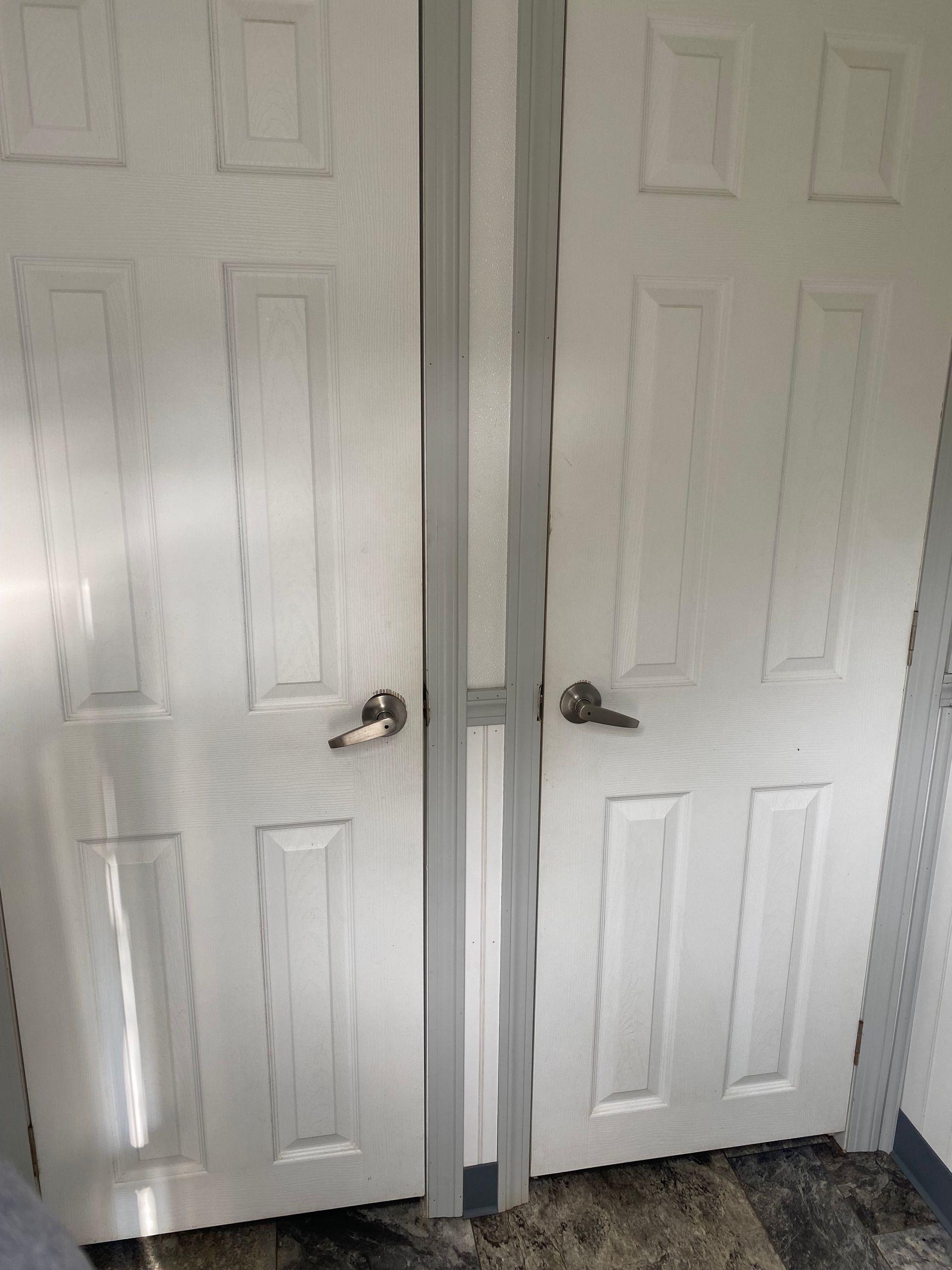 White double closet doors with silver handles, slightly open in a hallway.