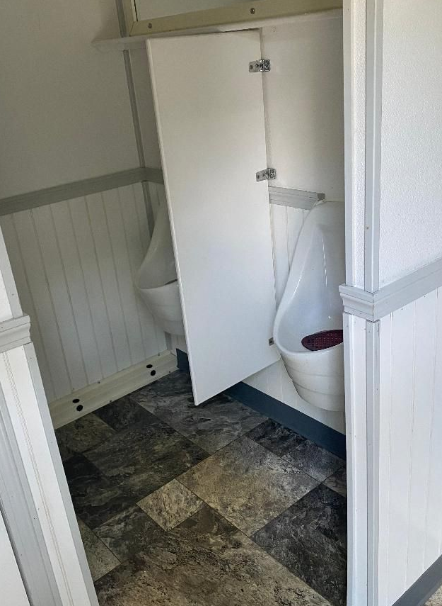 Small bathroom with a toilet partially hidden by an open cabinet door and dark tiled floor.