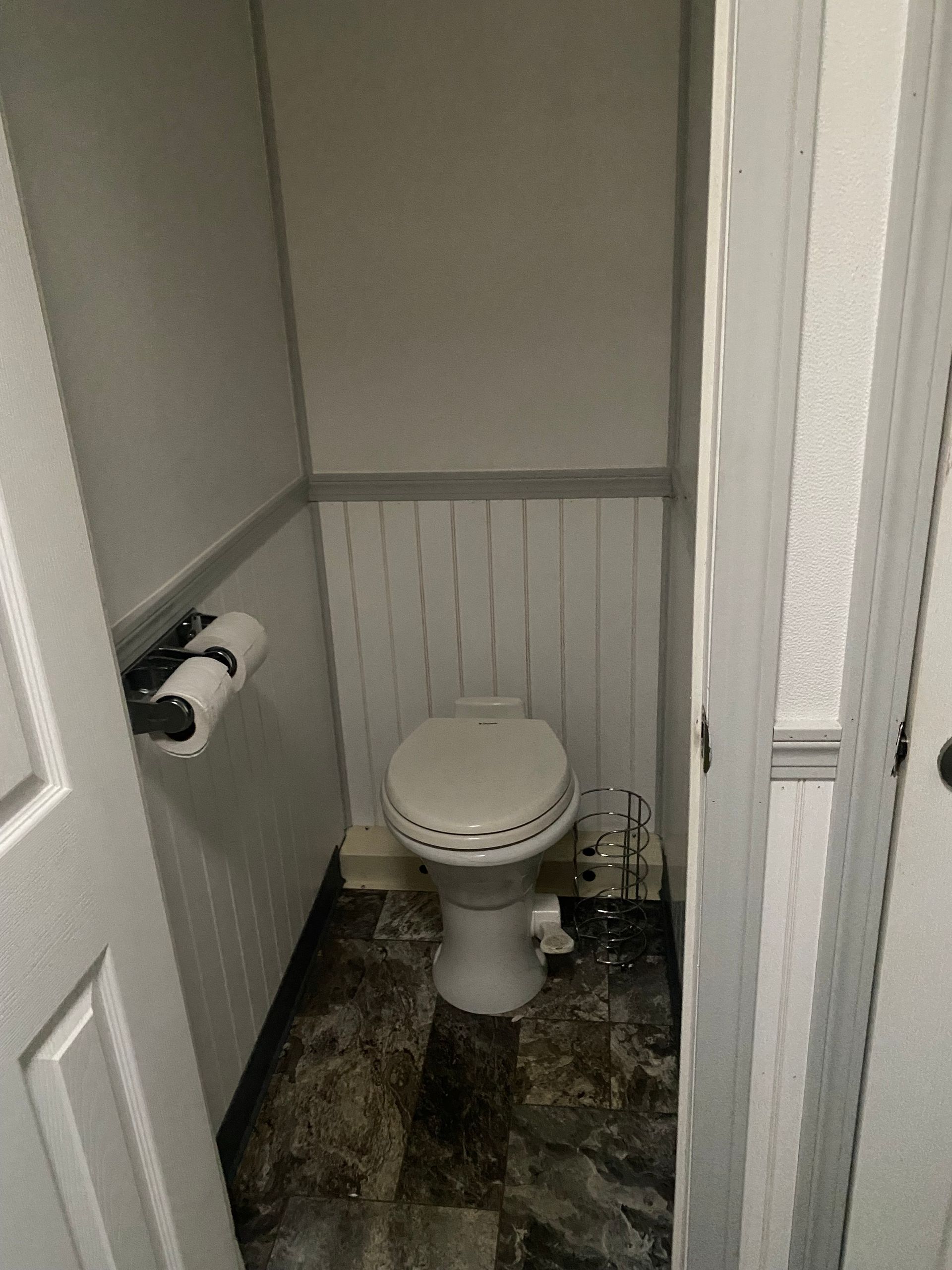 Small bathroom with a toilet, white wainscoting, and a wall-mounted toilet paper holder.