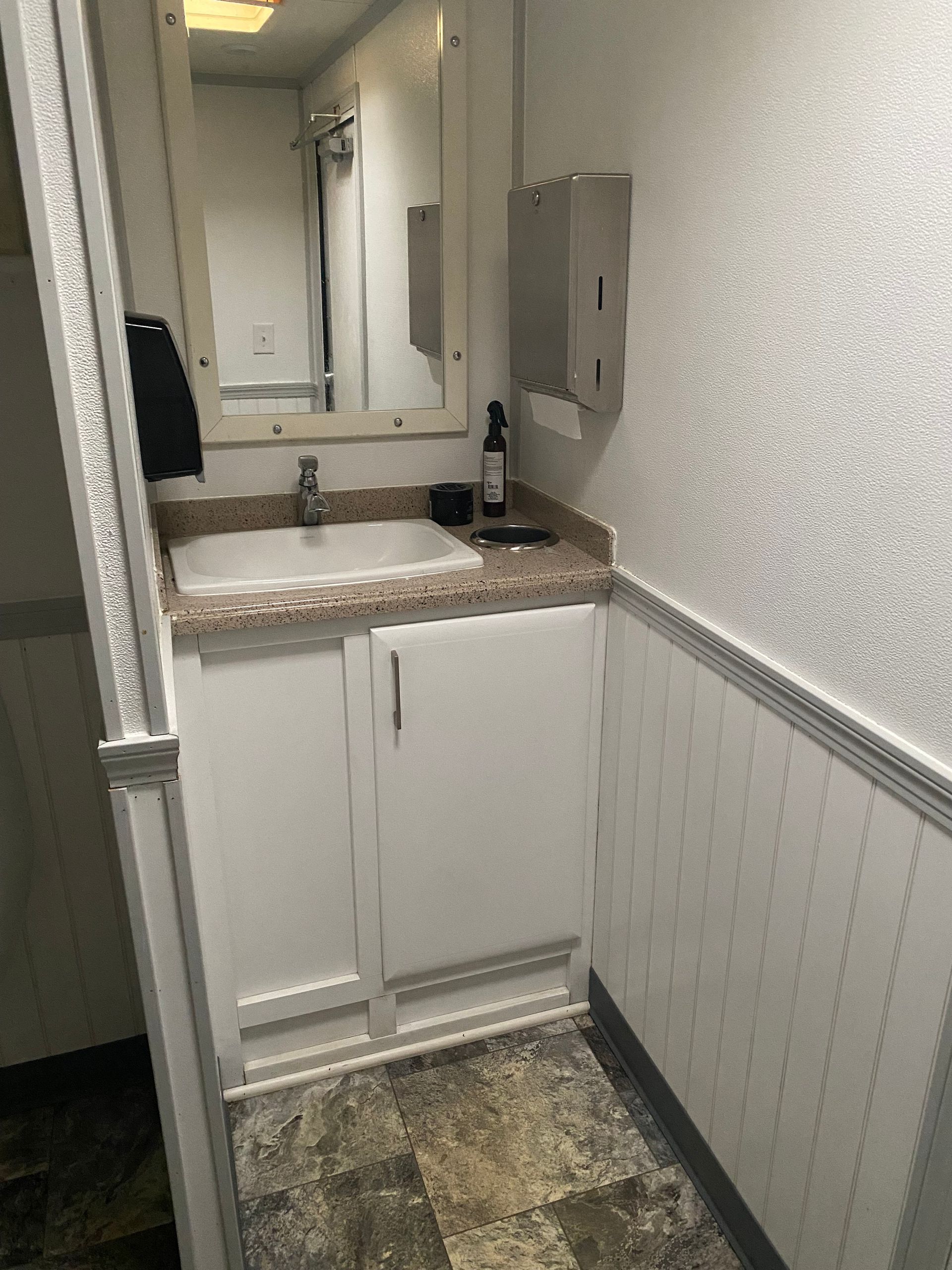 Narrow bathroom vanity with sink, mirror, and white wainscoting in a small hallway alcove
