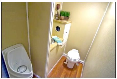 Tiny beige bathroom with a toilet, sink, mirror, and wooden floor.