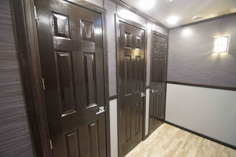 Hallway with three dark wooden doors, light wood flooring, and wall sconces
