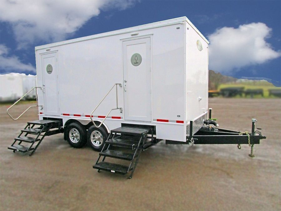 White mobile trailer with two side ramps on a paved lot under a cloudy sky
