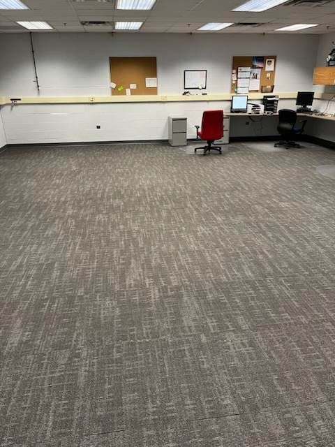 An empty office with a carpeted floor and a red chair.