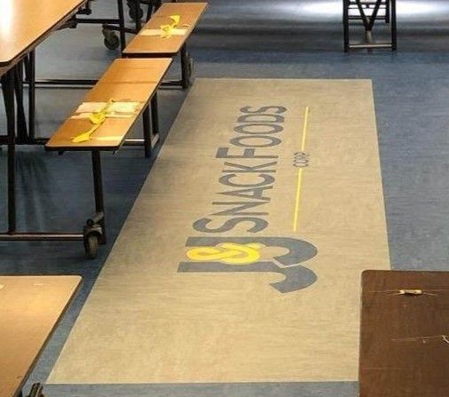 A snack foods logo is painted on the floor of a school cafeteria