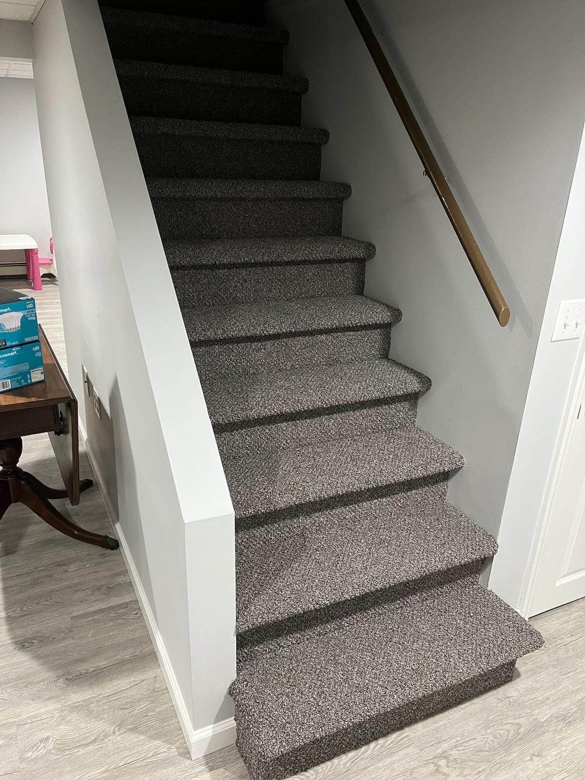 A staircase with carpeted steps and a wooden railing in a basement.