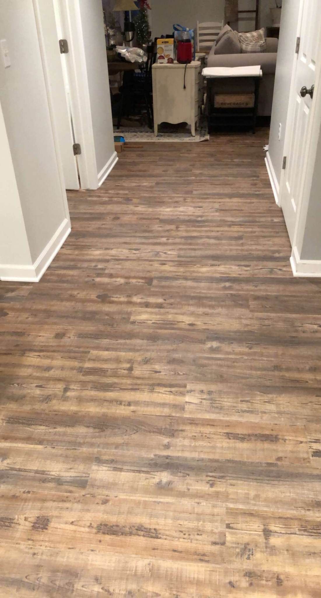 A hallway with a wooden floor and a living room in the background.