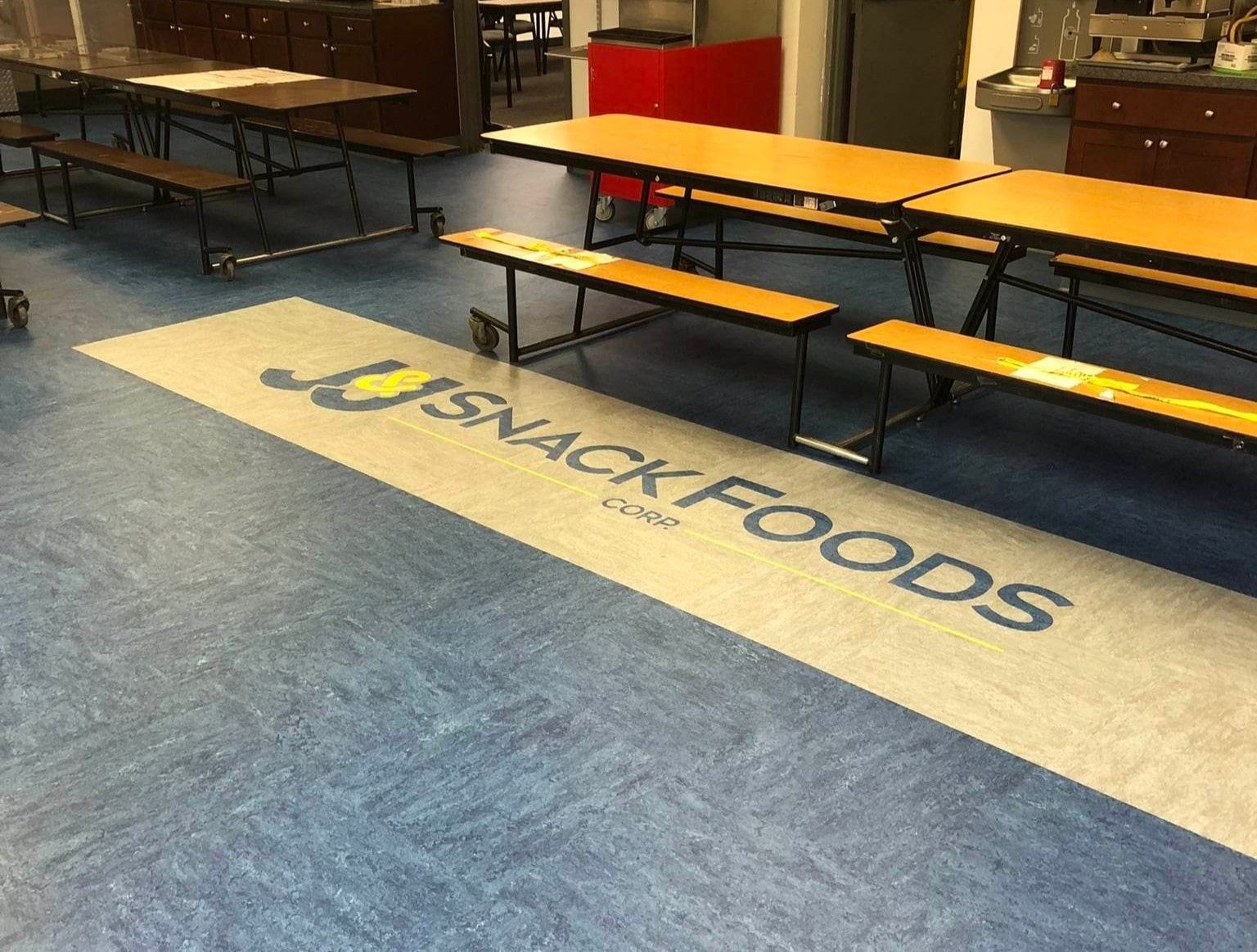 A school cafeteria with tables and benches and a snack foods logo on the floor.