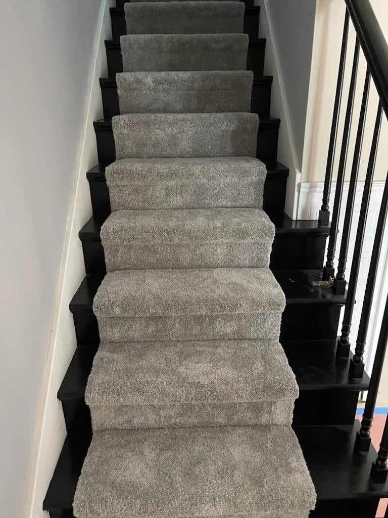 A staircase with a gray carpet on the steps and a black railing.