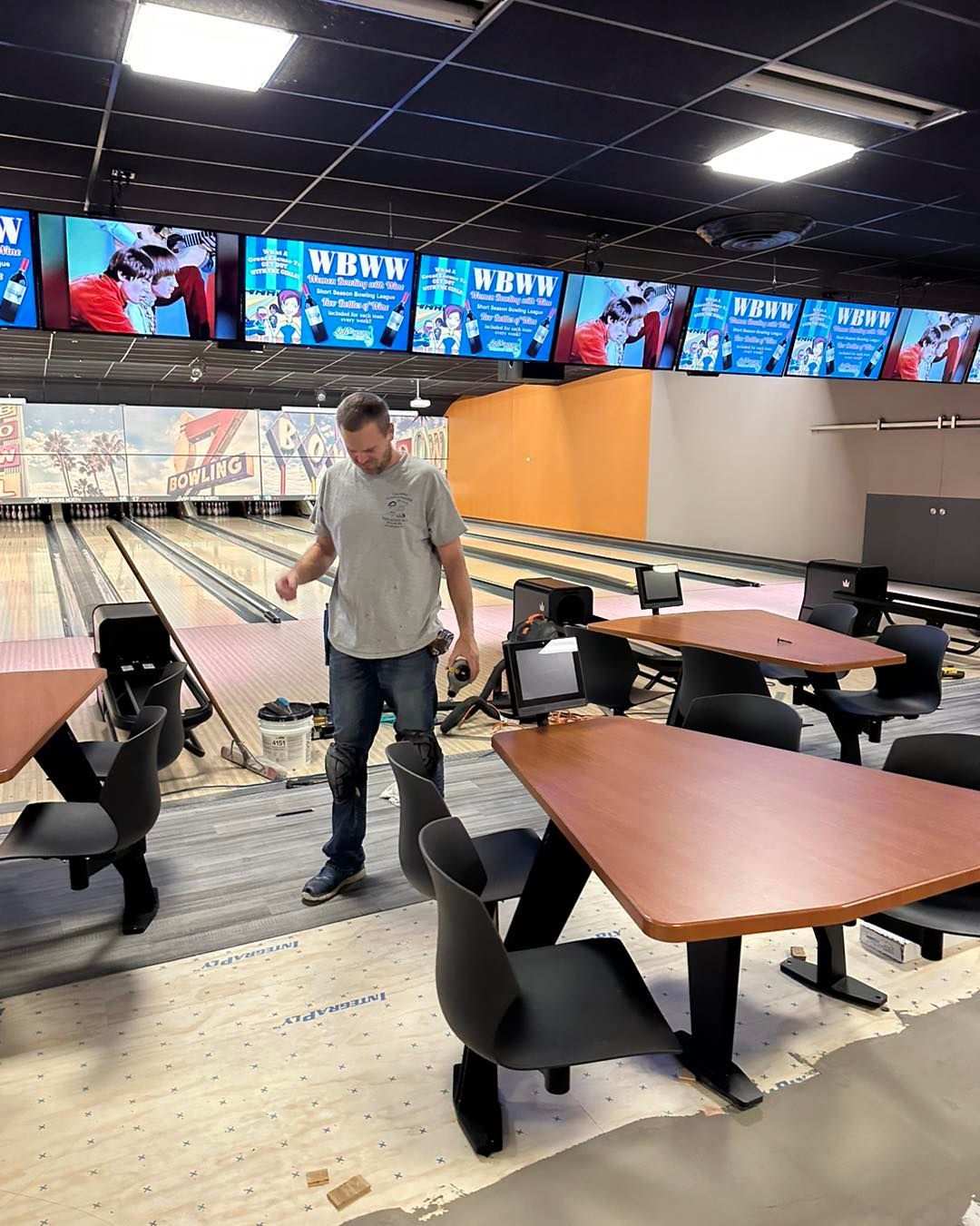 A man is standing in a bowling alley with tables and chairs.
