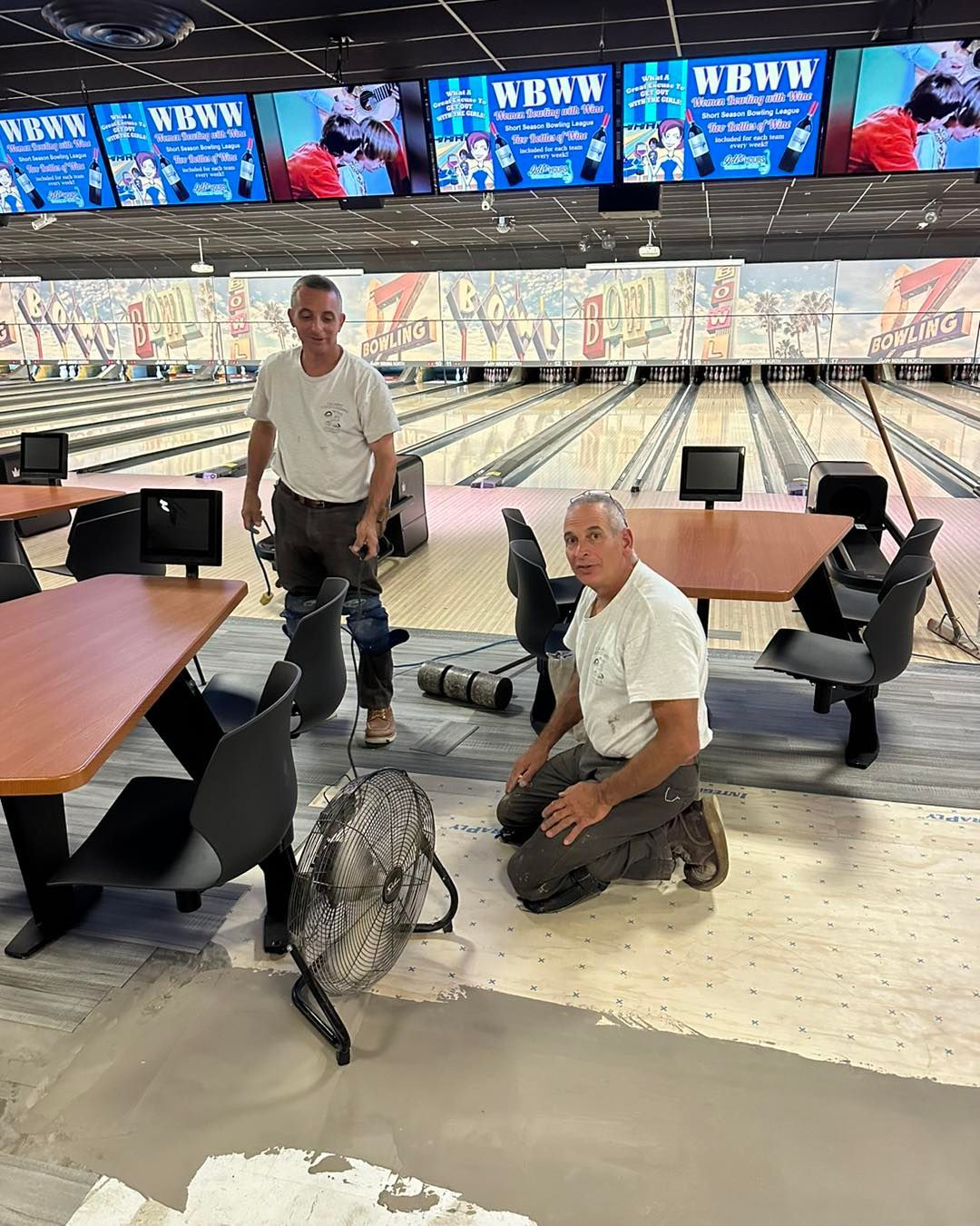 Two men are kneeling down in a bowling alley.