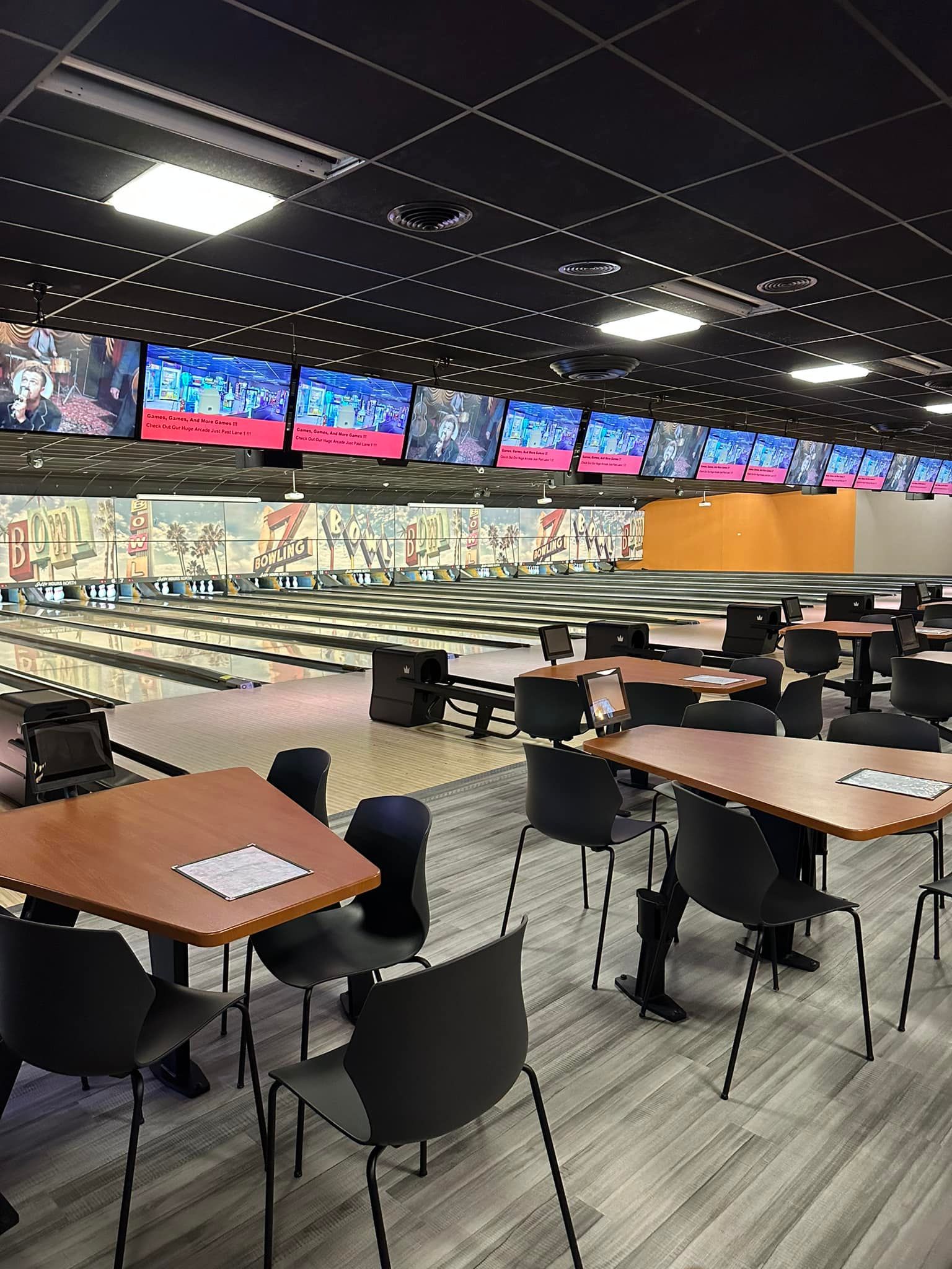 A bowling alley with tables and chairs and a bowling alley in the background.