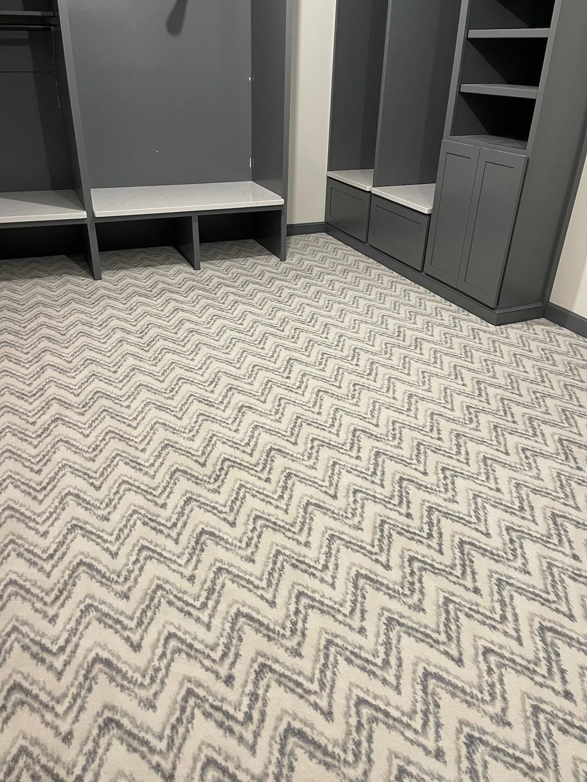 A closet with a chevron patterned carpet and gray cabinets.
