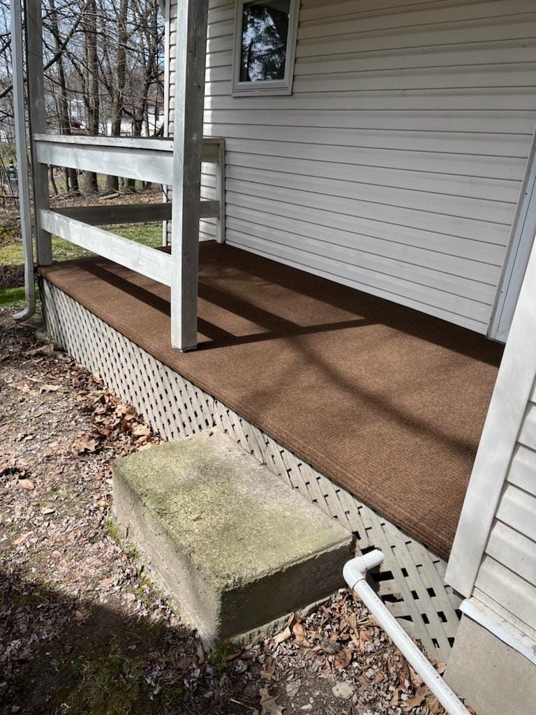 A porch with a wooden railing and a brown carpet on it.