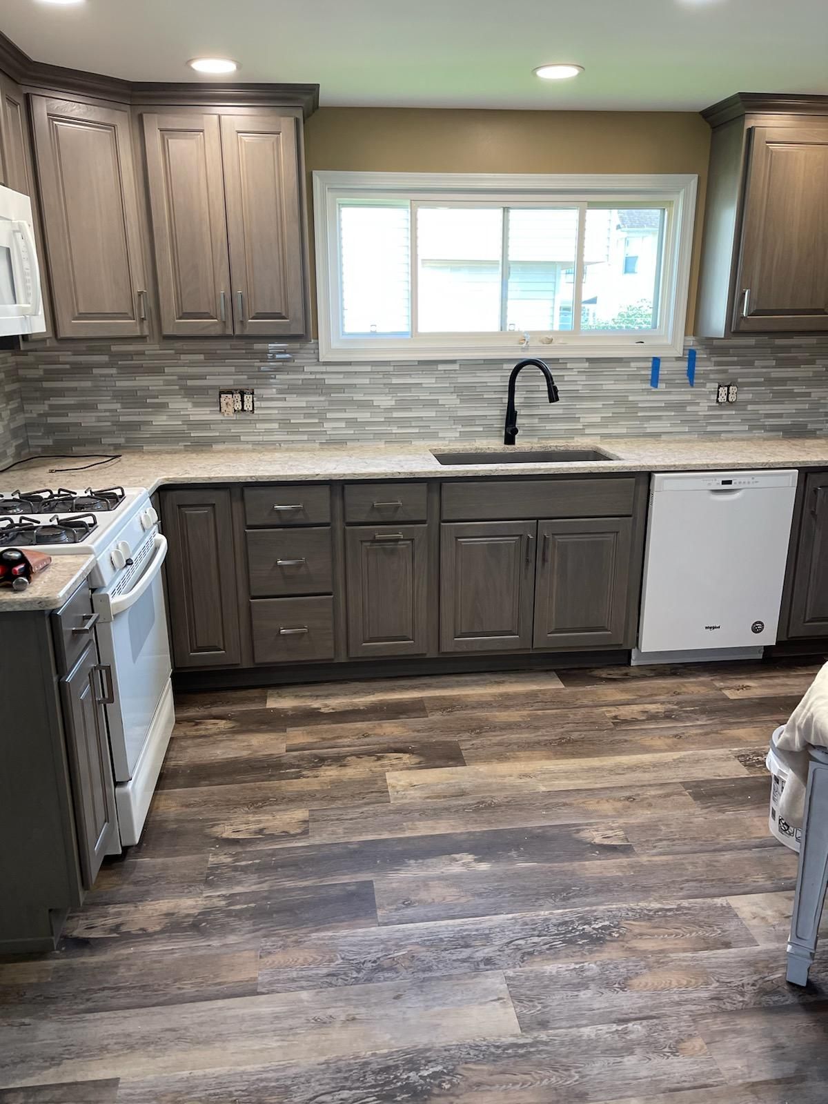 A kitchen with gray cabinets , white appliances , a sink , and a window.