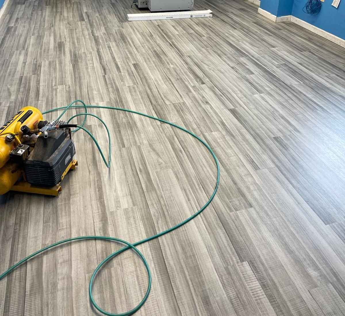 A vacuum cleaner is sitting on a wooden floor next to a green hose.