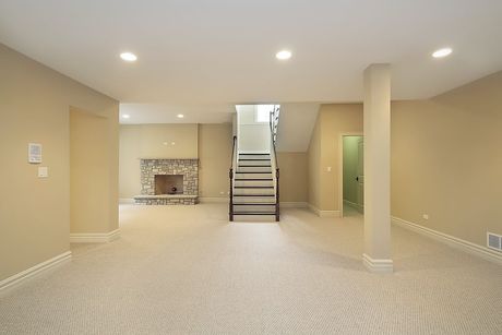 An empty basement with a fireplace and stairs.