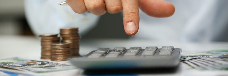 A person is using a calculator next to a pile of coins.