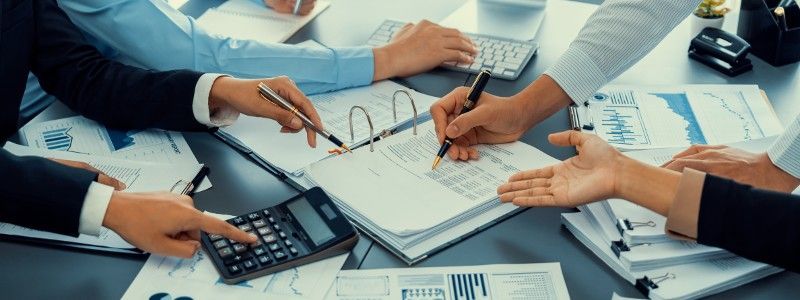 A group of people are sitting around a table with papers and a calculator.