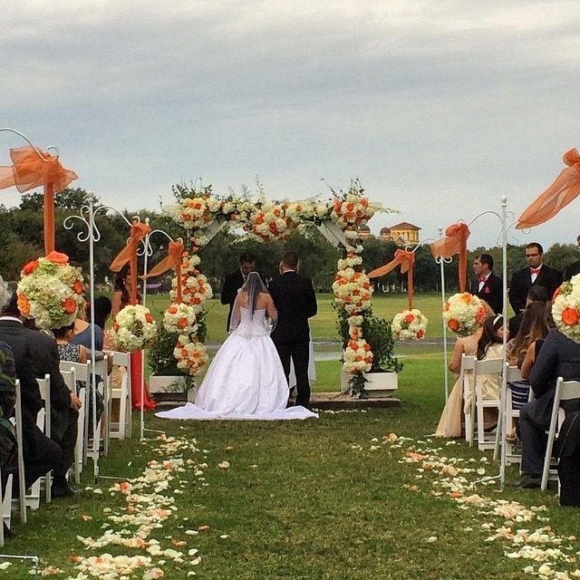 White wedding aisle with chairs leading to an altar under a tented canopy and floral petals along the floor