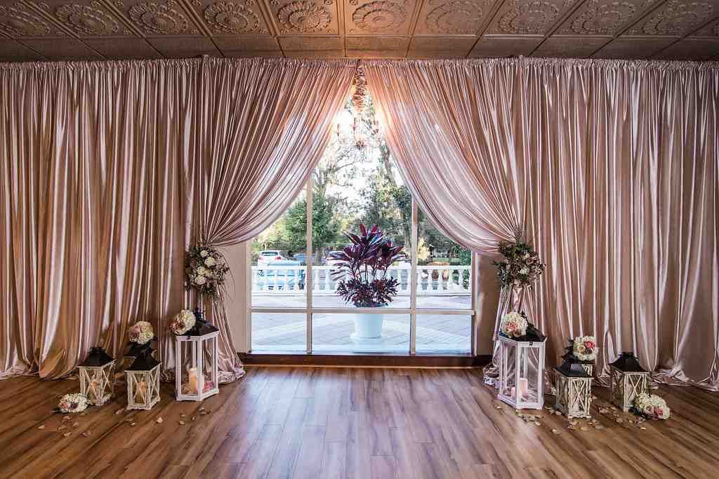 Decorated wedding venue with draped curtains, floral arrangements, and sliding glass doors to a garden